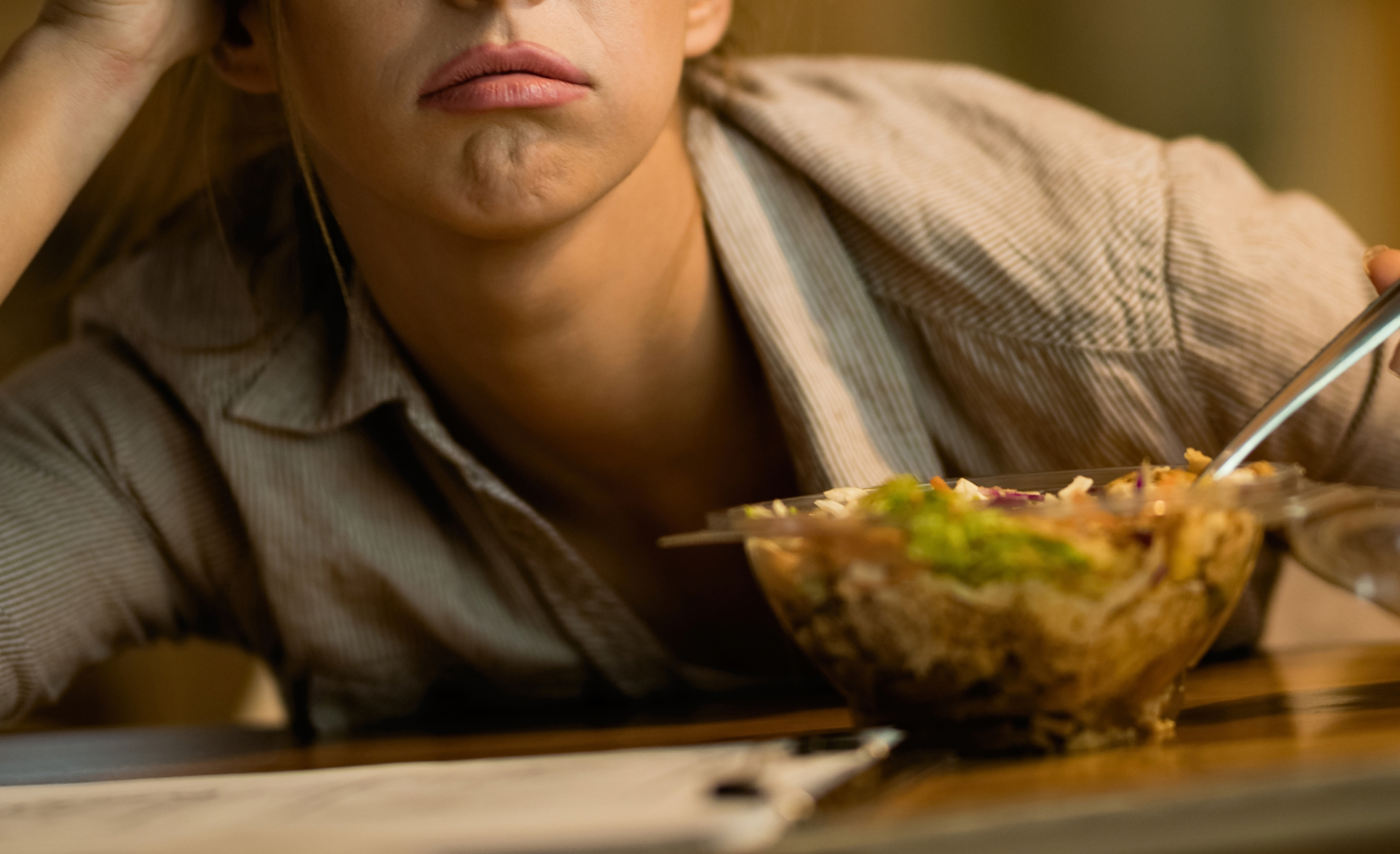 A close-up of a person leaning over a table with a concerned expression, with a salad bowl in front, indicating issues related to rapid weight loss.