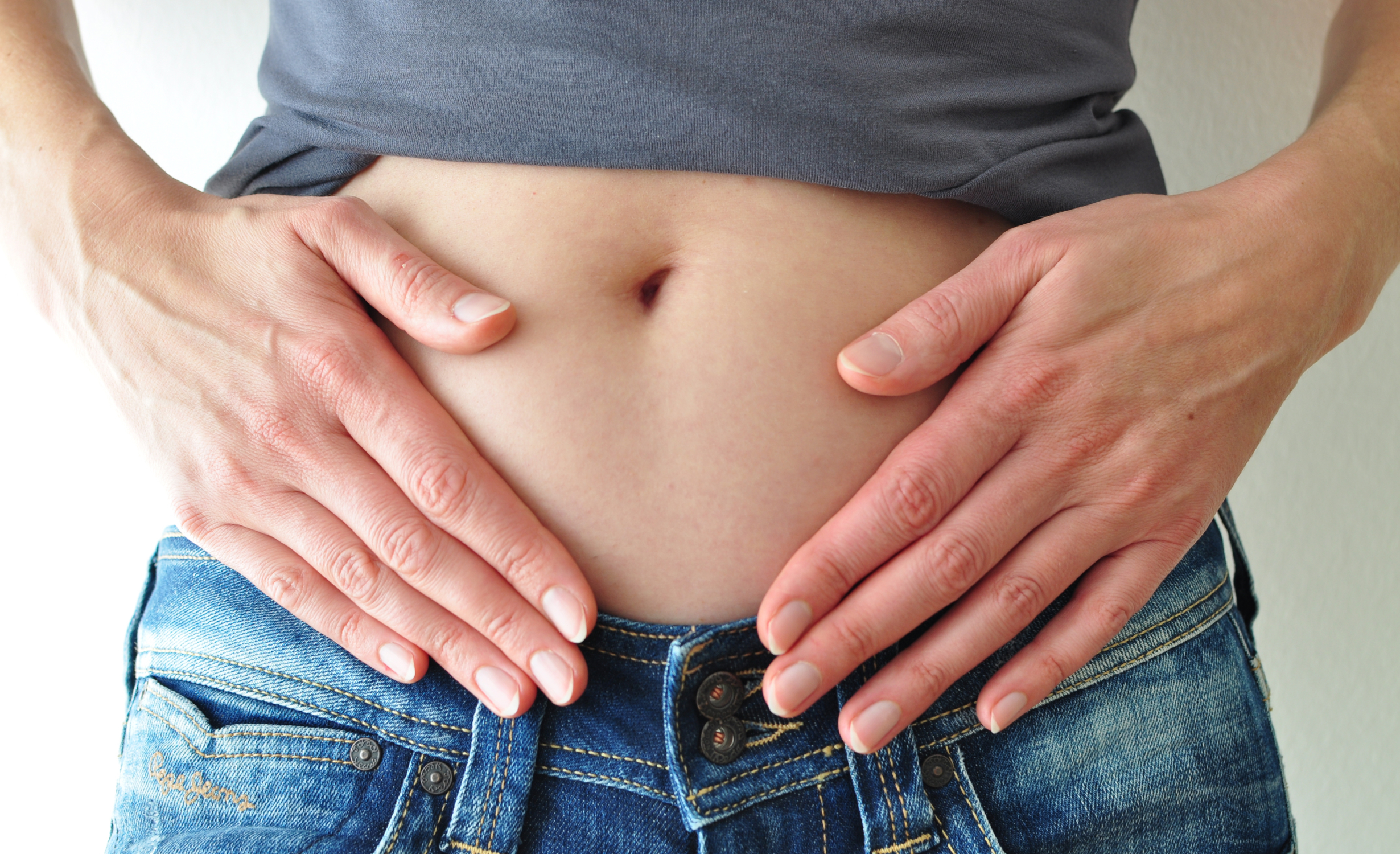 A close-up image of a person’s midsection with their hands resting on their bloated stomach, illustrating symptoms of stomach bloating conditions.